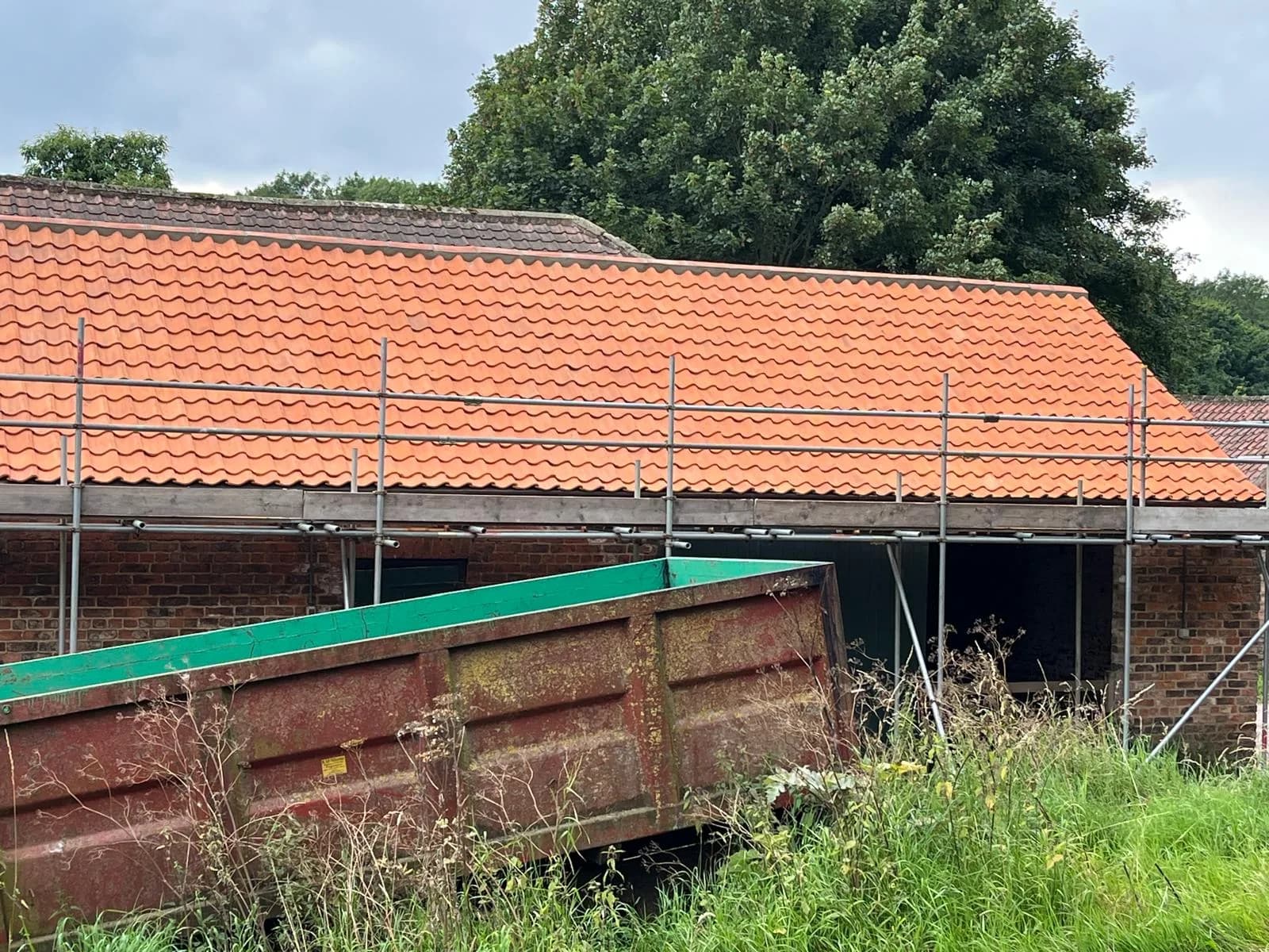 Rural barn with a new clay pantile roof, scaffolding along the front and new green doors completing the brick elevation.
