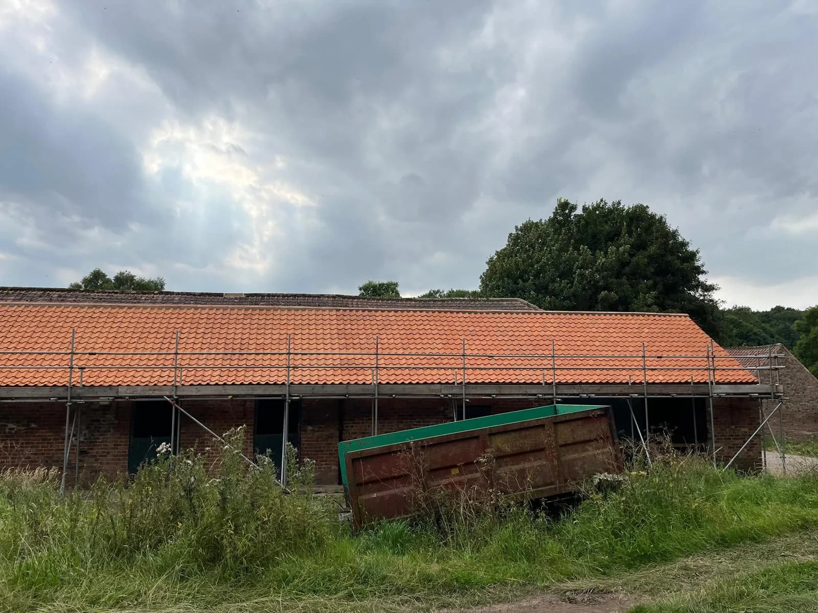 Completed clay pantile re-roof on a rural agricultural barn, scaffolding still in place under a dramatic North East sky.