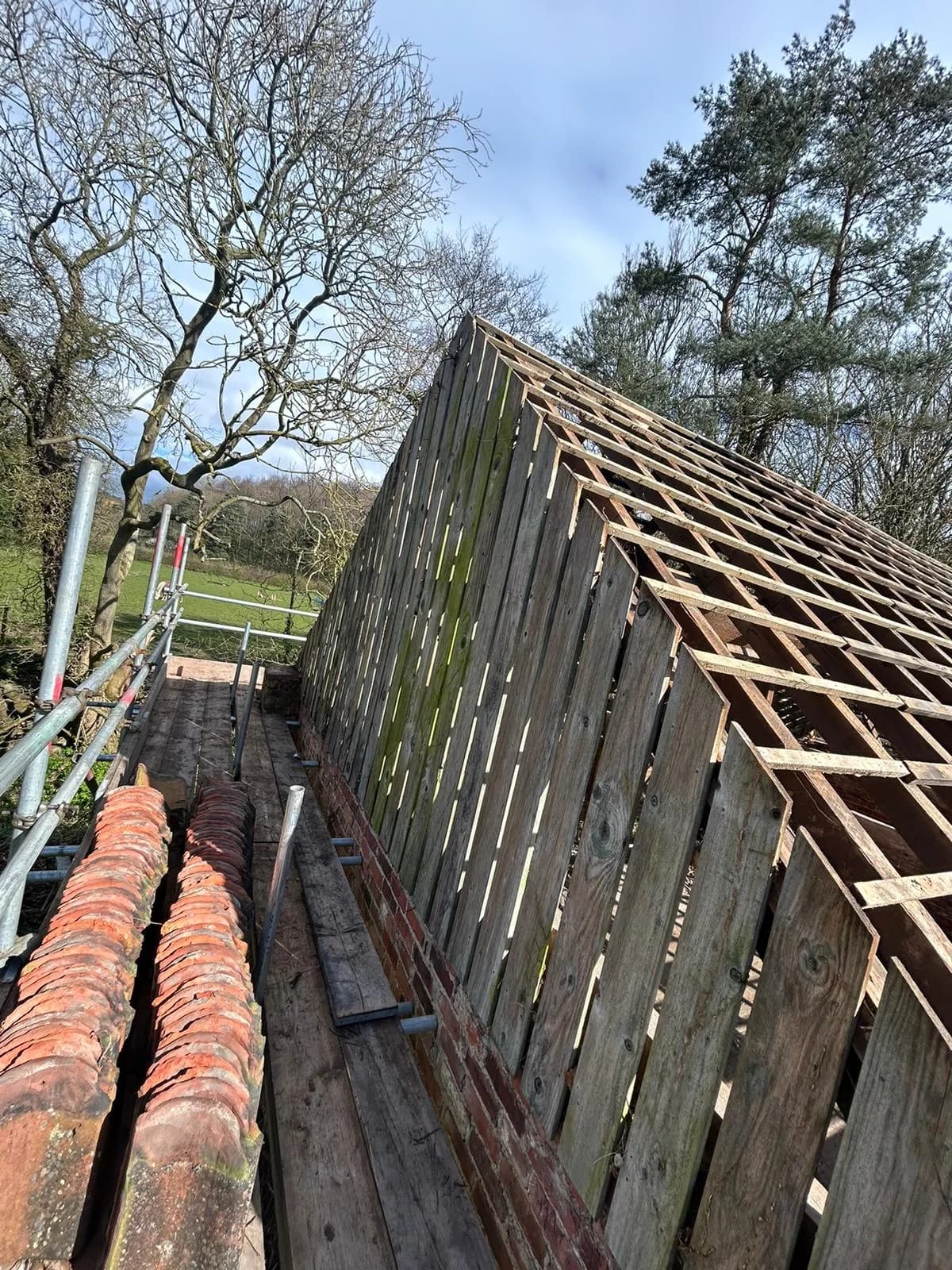 Roof stripped to bare battens with clay pantiles staged on the scaffold board, ready for laying the new covering.