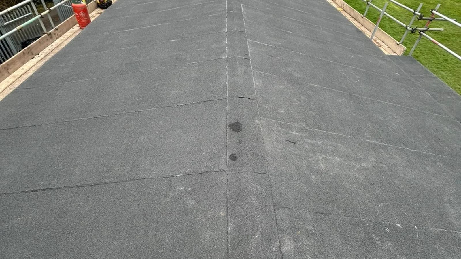 Completed long flat-felt roof on a two-storey building with scaffolding around the perimeter and terraced housing beyond — commercial flat roofing Northeast England
