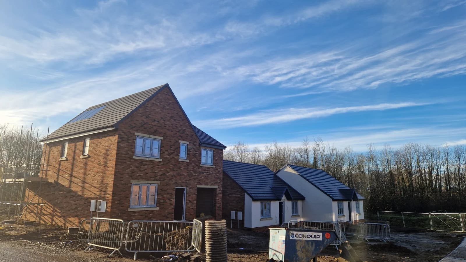 New-build detached homes with dark plain-tile pitched roofs against blue sky — commercial roofing for housing developers, Northeast England