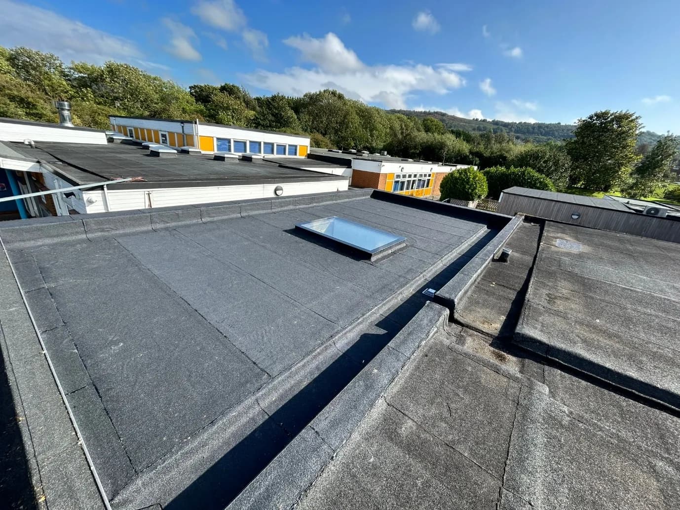 Completed built-up warm flat roof with rooflight on the Normanby Primary School extension in Middlesbrough, with the school buildings and hills behind.