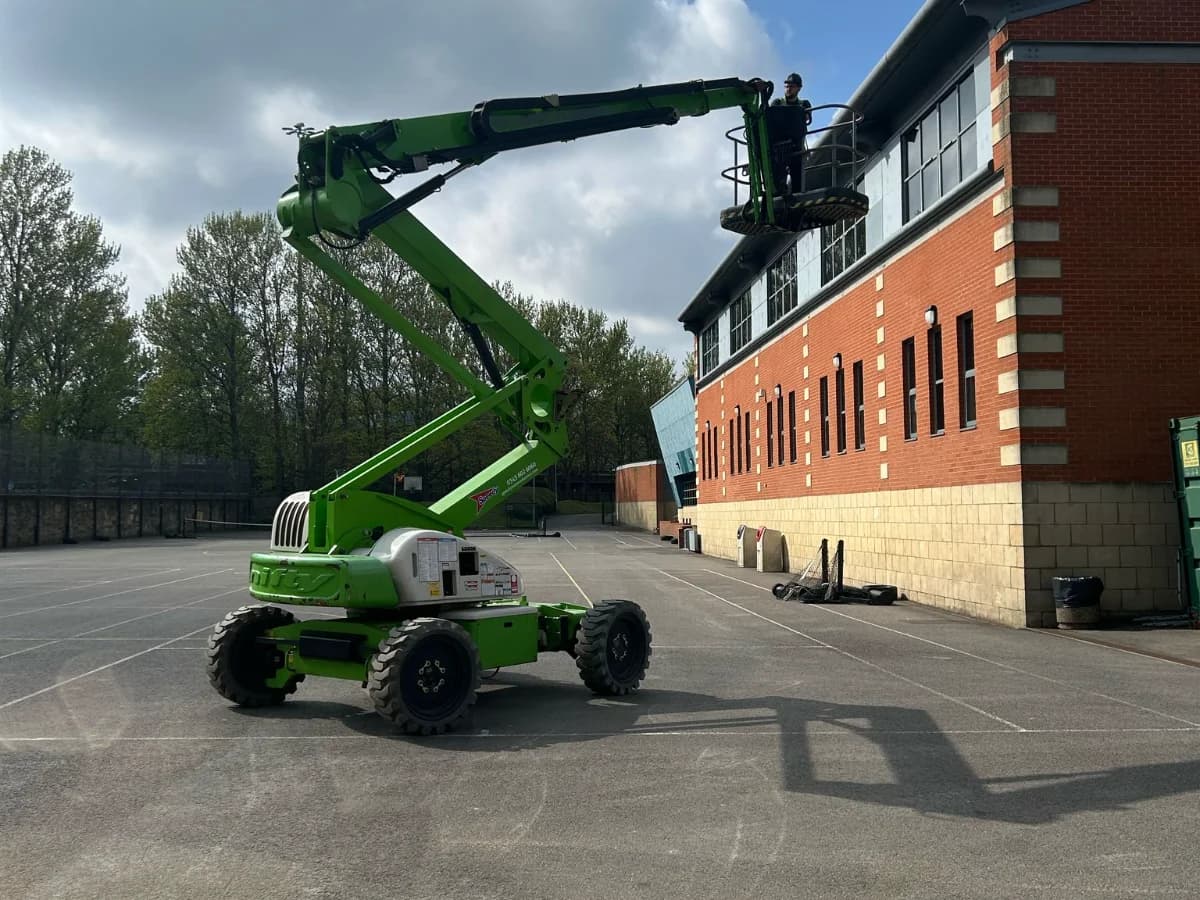 Articulated boom platform reaching a two-storey red brick commercial building roof under blue sky — commercial roofing contractor County Durham