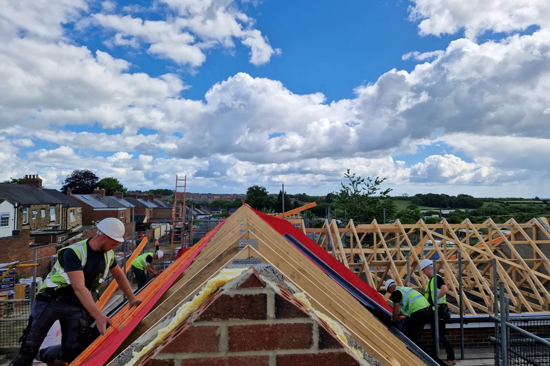 Four-person Evenii team in branded hi-vis installing a new-build pitched roof on a clear day — new-build roofing contractor for housing developers